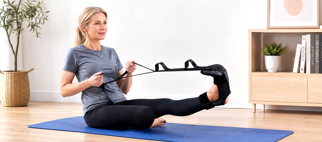Woman stretching with a strap while seated on an exercise mat